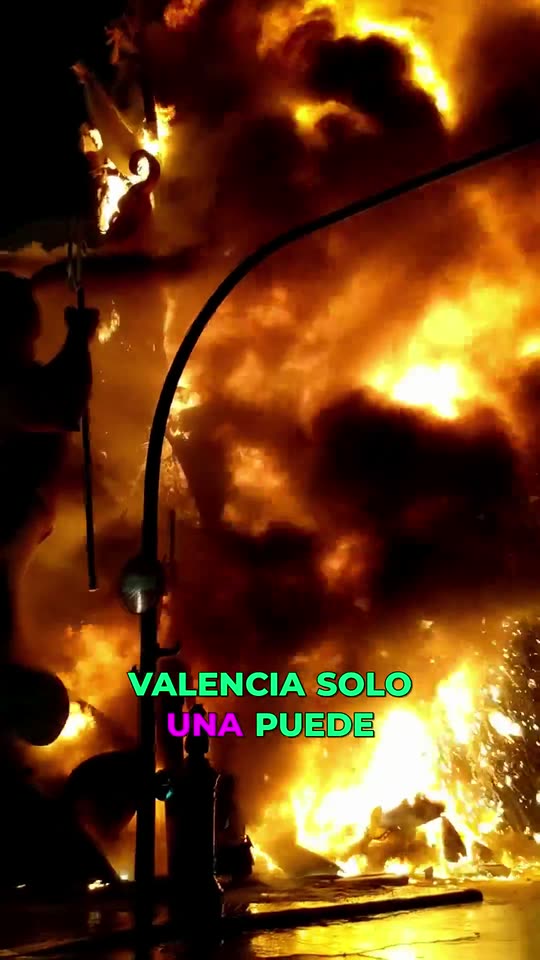 Vertical Short: a multi-storey Fallas figure burning in a Valencia street at night, with a burned-in Spanish caption.